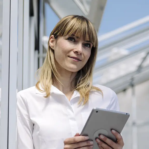 Thoughtful businesswoman holding digital tablet while standing by wall 