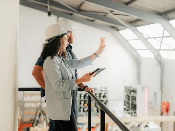 Woman and man with hard hats discussing in a factory