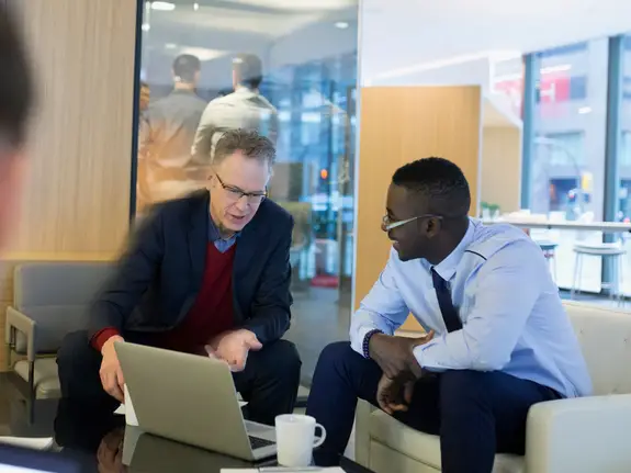 two businessmen smiling and talking while looking at laptop
