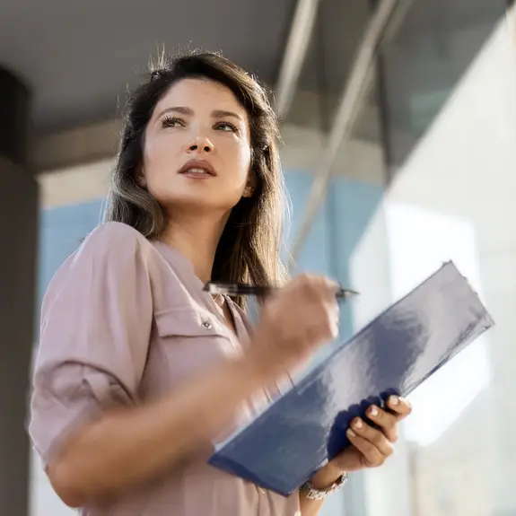 woman wearing a pink blouse taking notes outside of her office building